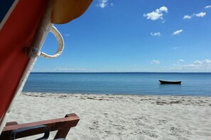 Blick auf einen Strand mit einem Boot auf dem Wasser und einem Strandsonnenschirm.