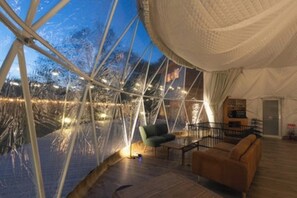 Estructura cubierta con una terraza de madera, un sofá y una escalera que conduce a un nivel superior.