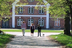 A pathway leading to a brick building with multiple windows and a dog on a leash. - Holiday apartment with 1 bedroom (Stoltenberg)