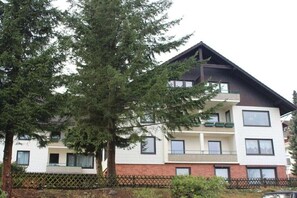 Ein mehrstöckiges Wohngebäude mit Balkonen, einem sichtbaren Fenster und einem Baum im Vordergrund.