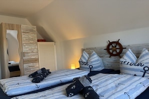 Ein Schlafzimmer mit einem Bett, einem hölzernen Kleiderschrank, einem an der Wand befestigten Schiffsschwengel und gestreiften Kissen.