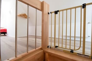 Ein Zimmer mit einem Fenster aus Holzrahmen, einem Metallgitter und einem roten Stuhl im Hintergrund.