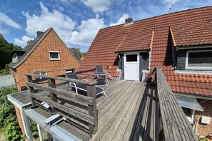 Ein Wohnhaus mit Holzterrasse, Backsteinfassade und rotem Ziegeldach.