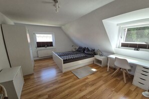 Ein Schlafzimmer mit Bett, Schreibtisch, Stuhl, Fenster und Heizkörper.