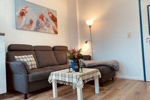 Ein Wohnzimmer mit einer Couch, einem Couchtisch mit Unterlage, einer Lampe und einem Bild an der Wand.