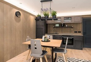 Eine moderne Küche mit Holzverkleidung, einem Esstisch mit Stühlen, einer Pendelleuchte und eingebauten Schränken.
