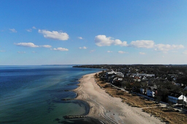Luftaufnahme einer Küstenstadt mit Strand, Häusern und blauem Himmel.