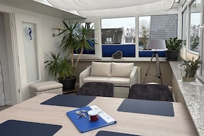 Ein Wintergarten mit Tisch, Stühlen, einer Couch und Topfpflanzen.