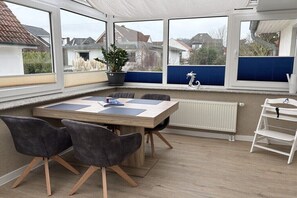 Ein Wintergarten mit Tisch und Stühlen, einer Topfpflanze und Blick auf die Nachbarschaft.