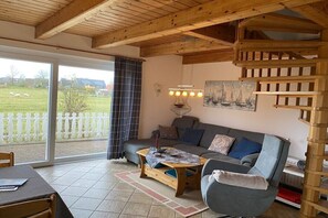 Ein gemütliches Wohnzimmer mit Holzboden, einer Couch, einem Couchtisch und Blick auf einen eingezäunten Außenbereich.