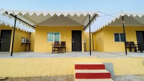 Un bâtiment jaune avec un porche couvert, deux portes et une petite table entourée de chaises.