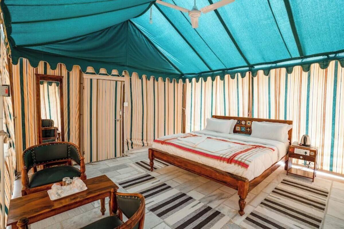 A tented room with a bed, a chair, a table, and a nightstand.