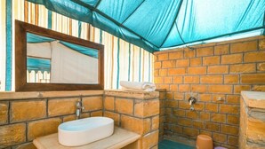 Une salle de bain équipée d’un lavabo, d’un miroir et d’un espace douche, avec des murs en briques et un auvent bleu.