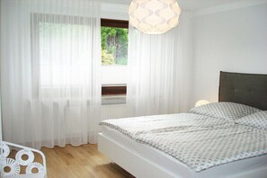 Ein Schlafzimmer mit Bett, weißen Vorhängen, einem Fenster mit Blick auf Grünflächen und einer Hängelampe.