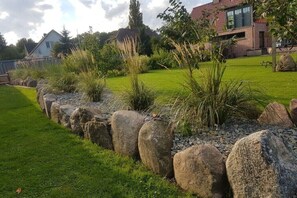 Ein Garten mit Steinrand, Rasenfläche und einem modernen Haus im Hintergrund.