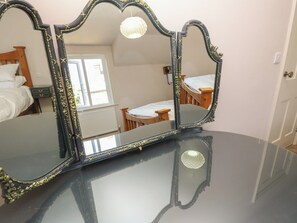 A room with a large mirror on a glossy black surface, a wooden bed, a small table, and a window with daylight coming through. - 8 Manor Villas (Totland Bay)