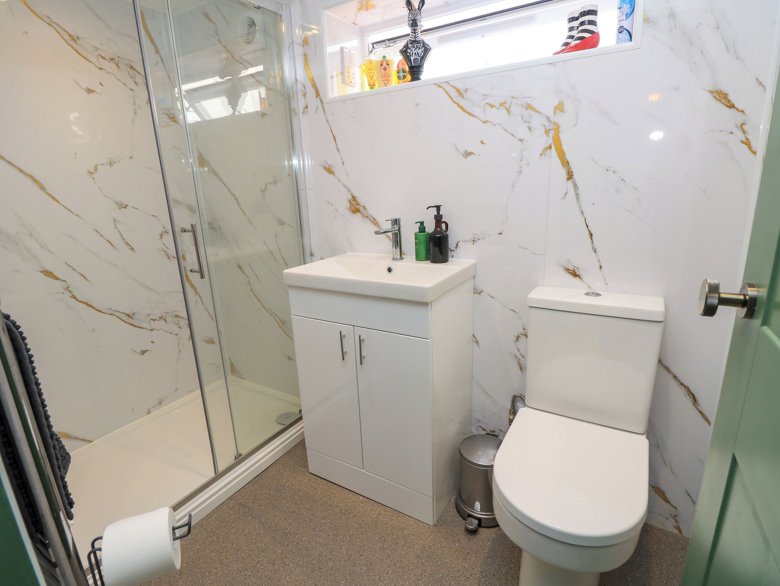 Une salle de bain avec une douche à parois de verre, un lavabo blanc avec un miroir au-dessus et des toilettes.