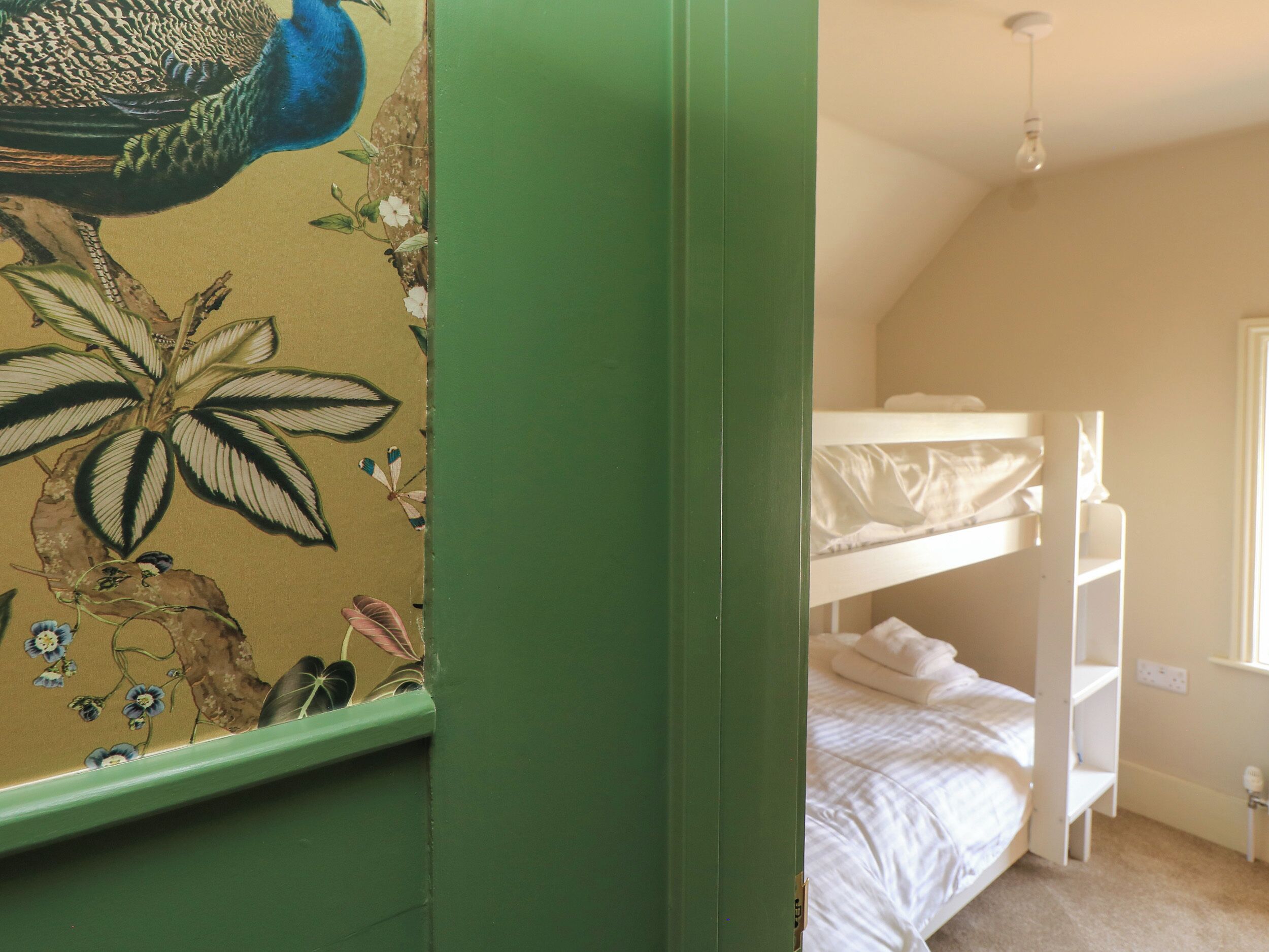 A bunk bed in a room with a green wall and a mural of a peacock and flowers.