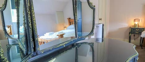 A room with a large mirror, a bed, a bedside table with a lamp, and a wall-mounted heater.