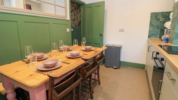 Un coin repas avec une table en bois, dressée pour quatre personnes, des chaises et un petit réfrigérateur.