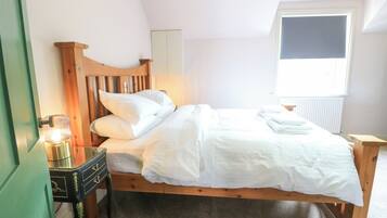 A bedroom with a wooden bed, a bedside table with a lamp, a radiator, and a window.