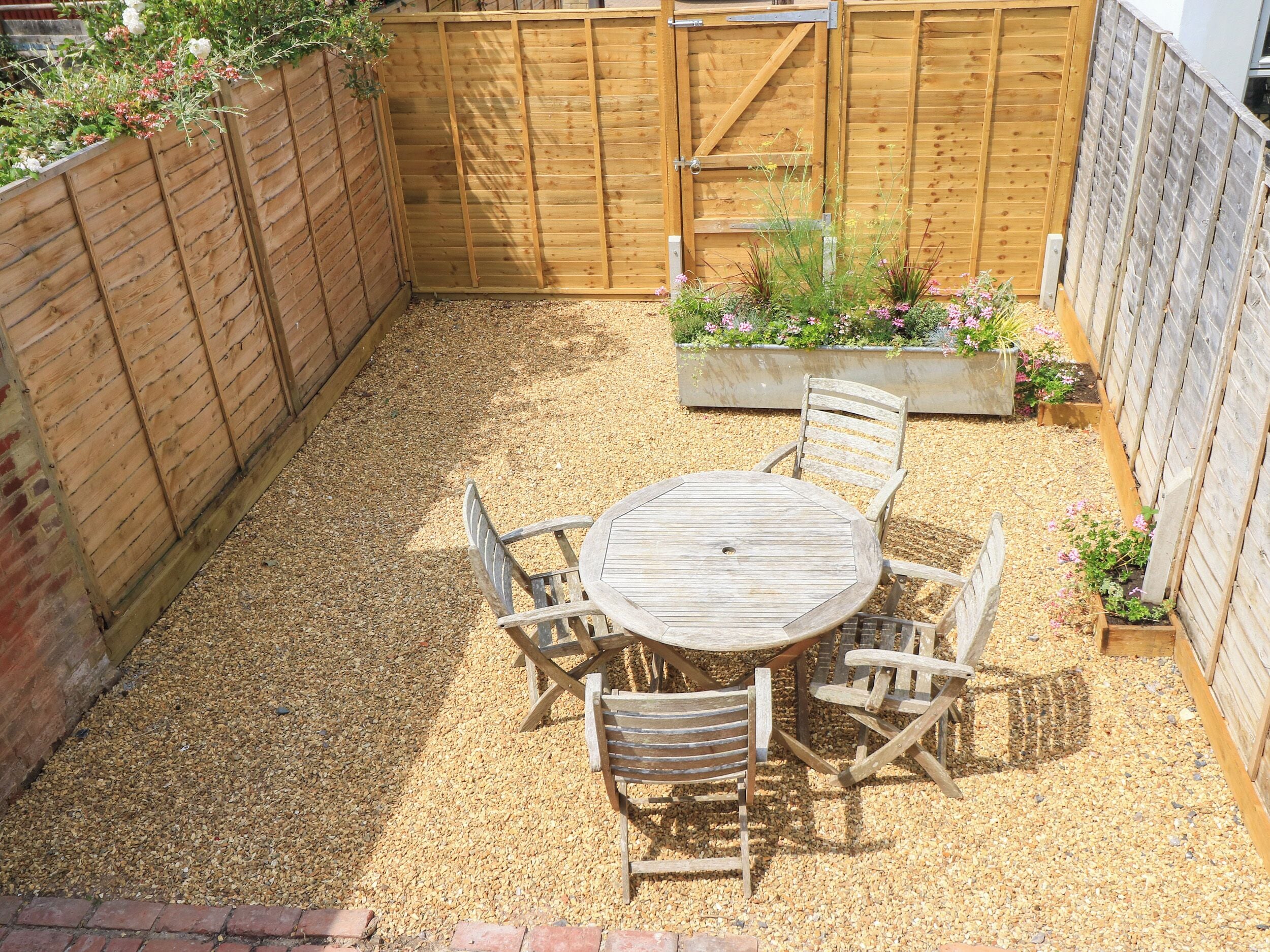 A wooden table and chairs in a garden area with a wooden fence and planters.