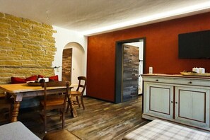 Ein Essbereich mit Holztisch und Stühlen, einer Steinwand und einer Küchenzeile mit weißem Schrank sowie einem Fernseher.