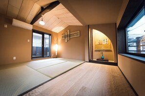 Ein Zimmer mit Tatami-Matten, einer Schiebetür, einer Wand-Klimaanlage, einer Stehlampe und einem kleinen Tisch mit einer Vase.
