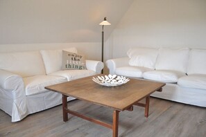 Ein weißes Sofa mit einem Kissen mit der Aufschrift 'enjoy the little things', ein Holztisch mit einer weißen Dekorationsschale und eine Stehlampe.
