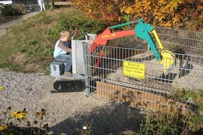 Eine Baustelle mit Metallzaun, einem gelb-grünen Bagger und einem Warnschild in deutscher Sprache.