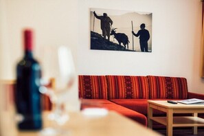 A living room with a red sofa, a wooden coffee table, and a painting of two people on a mountain. - Apartment with mountain view (Ladis)