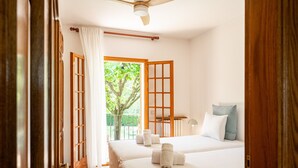 Ein Hotelzimmer mit zwei Betten, einem Deckenventilator, Blick auf Grünfläche und einem Balkon.