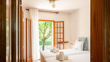 A hotel room with two beds, a ceiling fan, a view of greenery outside, and a balcony.