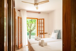 Habitación de hotel con dos camas, ventilador de techo, vista a zonas verdes y balcón.