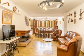 Una sala de estar con televisor, sofá de cuero, mesa de comedor y sillas.