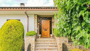 A stone house with a wooden door, stone steps, and a well-maintained hedge.