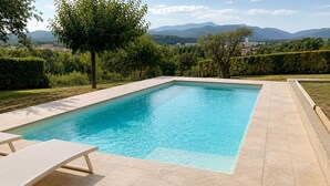 Ein rechteckiger Pool mit Fliesen umgeben, mit Grünflächen und Blick auf ferne Berge.