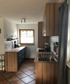 Een kleine keuken met houten kastjes, een raam, een spoelbak en een aanrecht.