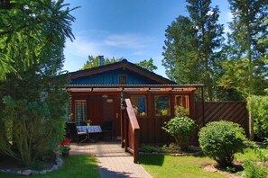 A wooden cabin with a covered porch, a table with chairs, and a garden path. - Holiday home in Warin with swimming pool (Warin)