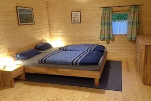 A wooden cabin room with a bed, two bedside tables, and a window with curtains. - Holiday home in Warin with swimming pool (Warin)