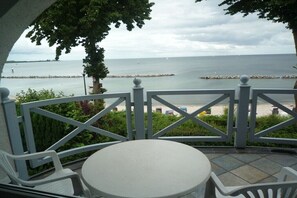 Ein Balkon mit weißem Tisch und Stühlen, mit Blick auf ein ruhiges Meer und einen steinernen Mole.