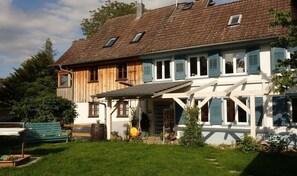 Ein zweistöckiges Haus mit Holzfassade, einer Veranda und einem kleinen Garten.