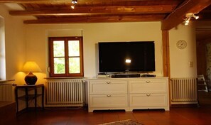 Ein Zimmer mit Fernseher auf einem Schrank, einem Fenster mit Blick auf Grünflächen, einer Heizung und einer Holzboden.