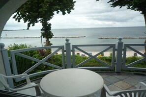 Ein Balkon mit Tisch und Stühlen, der Blick auf ein ruhiges Meer und eine felsige Küste freigibt.