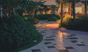 A pathway with a checkered pattern leading to a building with a fence and greenery. - Itadaki Suite (Phnom Penh)