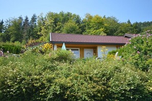 Ein Haus mit Ziegeldach, umgeben von üppiger Vegetation und blühenden Pflanzen.