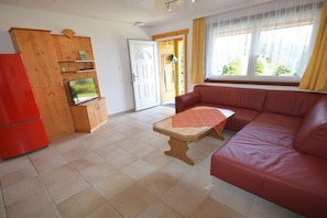 Ein Wohnzimmer mit einem roten Sofa, einem Holzschrank, einem roten Kühlschrank und einem Fenster mit Vorhängen.