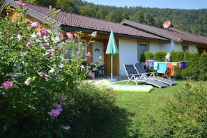 Ein Haus mit Ziegeldach, einem grünen Sonnenschirm, Sitzgelegenheiten im Freien und einer Sat-Anlage.