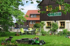 Ein traditionelles Gebäude mit einem Schild, das 'WANDSCHUHTTE WALTERSDORF' anzeigt, und einer grünen Wiese mit Gartenmöbeln.