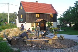A rustic wooden house with a red roof, a stone wall, and a paved area with benches and a fire pit. - Waltersdorf hiking hut (Bad Schandau OT Waltersdorf)